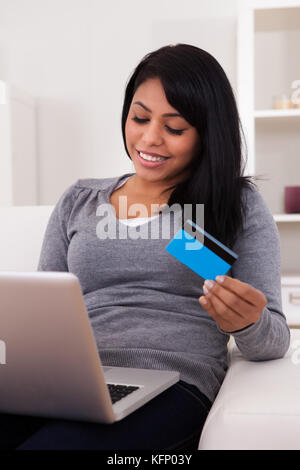 Glückliche junge Frau sitzt auf der Couch und online einkaufen Stockfoto