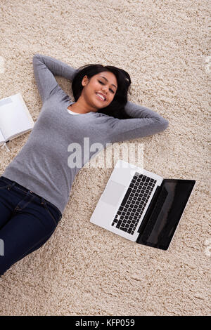 Blick von oben auf die junge Frau auf dem Teppich liegend mit Laptop Stockfoto