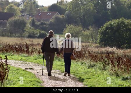 Kaukasische Paare mittleren Alters, vielleicht zurückgezogen, gehen Hand in Hand auf dem Fluss an der Wand im Waldringfield, Suffolk. Stockfoto