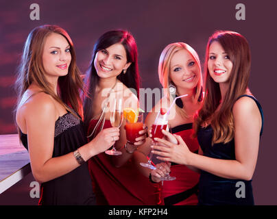 Gruppe von vier glückliche schöne junge Freundinnen feiern in einem Nachtclub mit Gläser cocktail in der Hand Stockfoto