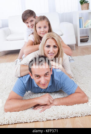 Glückliche Familie mit zwei Kindern liegen gehäuft auf dem Teppich im Wohnzimmer zu Hause Stockfoto