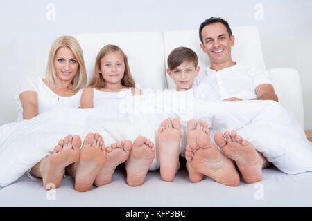 Glückliche Familie mit zwei Kindern im Bett unter dem Deckmantel zeigt Füße, drinnen Stockfoto