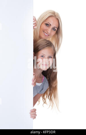 Porträt der Mutter und Mädchen guckt hinter Blank Board auf weißem Hintergrund Stockfoto