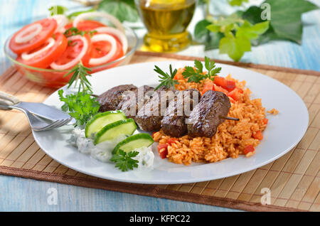 Griechische Frikadellen mit Paprika Reis und tsatsiki, im Hintergrund Tomatensalat mit Zwiebelringen. Stockfoto