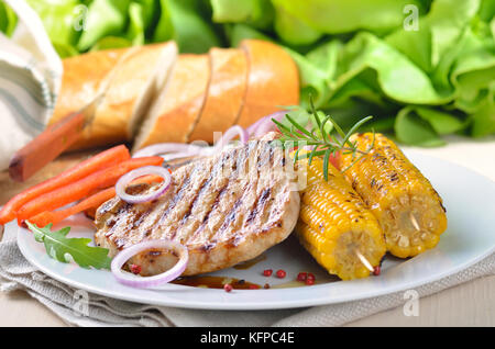 Heiß, lecker, lecker Gegrilltem Schweinefleisch Steak essen mit Mais, Zwiebeln, Paprika und Salat und Brot im Hintergrund Stockfoto