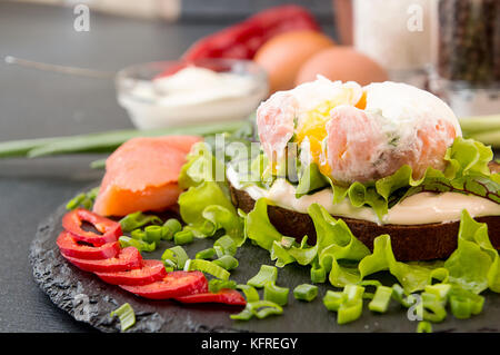 Toast mit Lachs, Pfeffer, Frischkäse, Schnittlauch und pochiertem Ei auf schwarzem Schiefer. Gesunde Ernährung Konzept Stockfoto