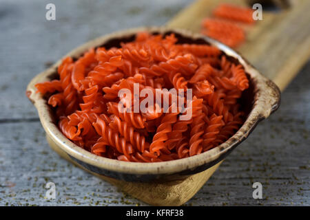 Nahaufnahme eines Steingut Schale voller ungekochte rote Linsensuppe fusilli auf einem grauen rustikalen Holztisch Stockfoto