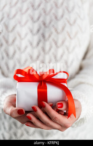 Der Frau mit roten Hände Maniküre, die kleinen weißen Geschenkbox mit roter Schleife Stockfoto