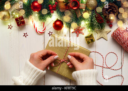 Der Frau die Hände binden bis Weihnachten Geschenk Box auf weiße Holztisch mit festlichen Dekorationen und Lichter Stockfoto