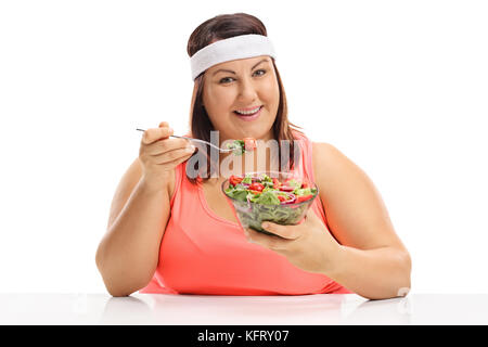 Übergewichtige Frau an einem Tisch sitzen und essen einen Salat auf weißem Hintergrund Stockfoto