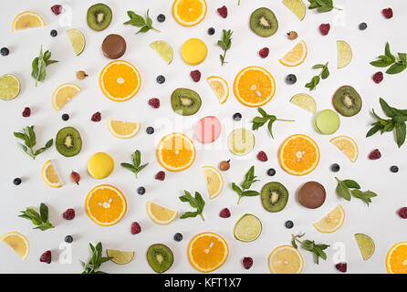 Flach Stillleben mit Macarons, Beeren, Minze und Zitrus- und andere Früchte: orange Frucht; Kalk; Zitrone, Kiwi auf weißem Hintergrund. Pop Art Trend noch Stockfoto