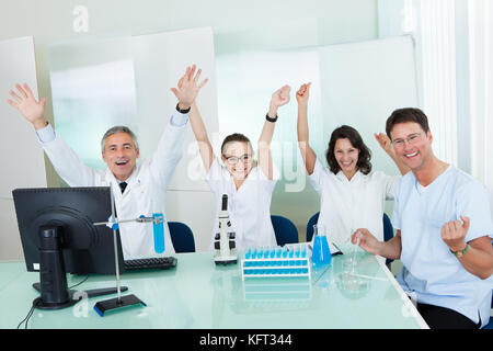 Laboranten oder medizinische Technologen um ein labortisch sitzen die Durchführung von Tests auf einem Rack von Reagenzgläsern Stockfoto