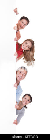 Zwei glückliche attraktive Paare im mittleren Alter einen Blank Board oder Plakat peering am Rand einer vertikalen banner Isolated On White Stockfoto
