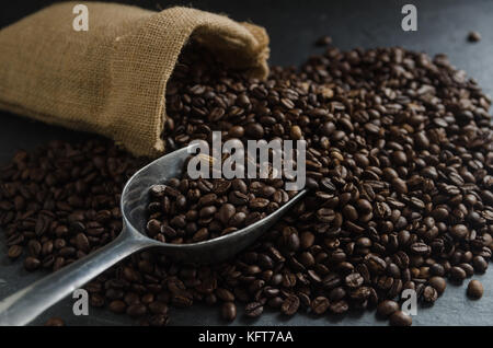 Kaffeetasse und gerösteten Kaffeebohnen in Sackleinen sack Sack mit Blätter auf schwarzem Granit Hintergrund Stockfoto