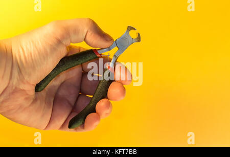 Hand, die kleine Kneifzange auf orange Hintergrund isoliert Stockfoto