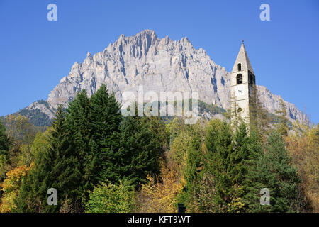 Glockenturm mit Herbstfarben im Vordergrund und einer massiven Klippe (Monte Bersaio) als Hintergrund. Sambuco, Provinz Cuneo, Piemont, Italien. Stockfoto