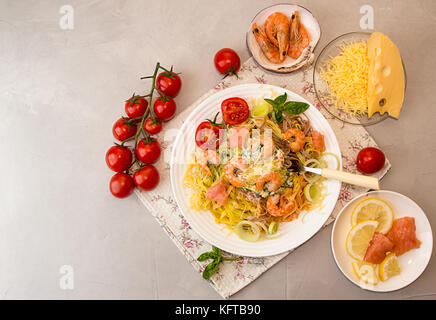 Overhead von Tisch. Pasta Tagliatelle mit gegrillten Garnelen, Lachs Fisch, Gouda Käse, mit Tomate Kirsche, Lauch, Basilikum servieren. Zutaten für ein Stockfoto