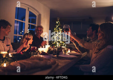 Erweiterte Familie toasten Wein zum Weihnachtsessen. Happy Family weihnachten Candle light Dinner zu geniessen zu Hause. Stockfoto
