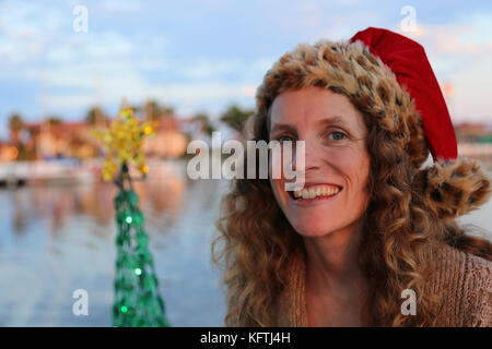 Junge Dame in einen festlichen Urlaub santa hat neben einem geschmückten Weihnachtsbaum. Stockfoto