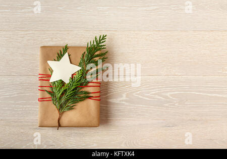 Weihnachten Geschenk in recycelten Verpackung Papier mit natürlichen Evergreen Dekorationen und eine leere umhüllt, sternförmige Geschenkanhänger auf Holz Hintergrund Stockfoto