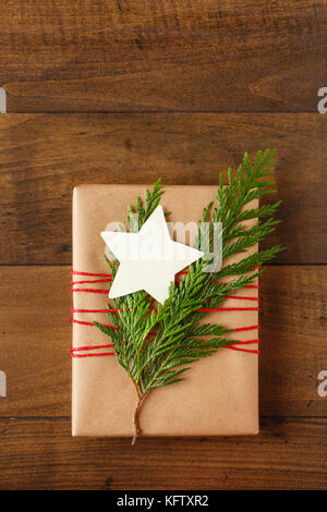 Weihnachten Geschenk in recycelten Verpackung Papier mit natürlichen Evergreen Dekorationen und eine leere umhüllt, sternförmige Geschenkanhänger auf Holz Hintergrund Stockfoto