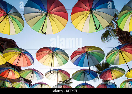 Bunte sonnenschirme Hintergrund. Multi-Schirme am Himmel schweben über der Straße gegen Palmen gefärbt. Regenschirm Straße Dekoration. Regenschirm S Stockfoto