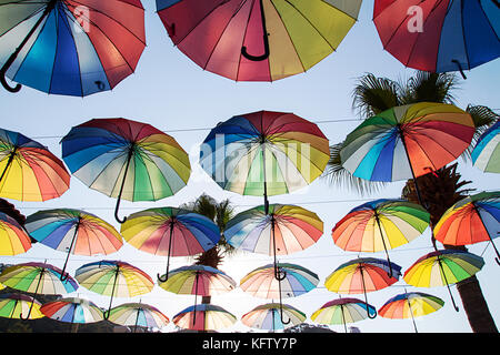 Bunte sonnenschirme Hintergrund. Multi-Schirme am Himmel schweben über der Straße gegen Palmen gefärbt. Regenschirm Straße Dekoration. Regenschirm Sk Stockfoto