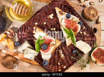 Overhead von Feigen, getrocknete Feigen, Snack sandviches mit Brie, Blau, Abb. Scheiben Käse, Pinienkerne, Blaubeere und Honig auf Holz- Hintergrund. Ansicht von oben. Sterben Stockfoto