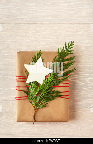 Weihnachten Geschenk in recycelten Verpackung Papier mit natürlichen Evergreen Dekorationen und eine leere umhüllt, sternförmige Geschenkanhänger auf Holz Hintergrund Stockfoto
