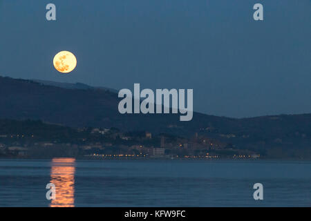 Wunderschöne Aussicht auf Vollmond gerade über Passignano (Umbrien), was auf dem Wasser des Lago Trasimeno Stockfoto