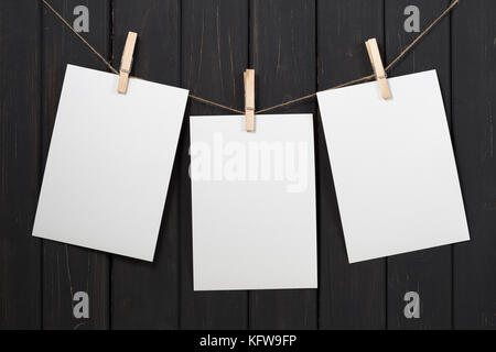 Drei leere weiße Papier Karten hängen am Seil mit Wäscheklammer auf schwarzem Holz- Hintergrund Stockfoto