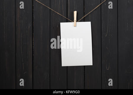 Leeres weißes Papier Karte hängen am Seil mit Wäscheklammer auf schwarzem Holz- Hintergrund Stockfoto