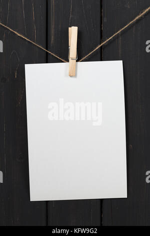 Leeres weißes Papier Karte hängen am Seil mit Wäscheklammer auf schwarzem Holz- Hintergrund Stockfoto
