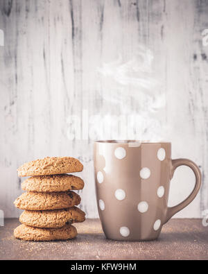 Stapel von oat Cookies und Polka Dot Becher mit heißem Getränk über Holz- Hintergrund Stockfoto