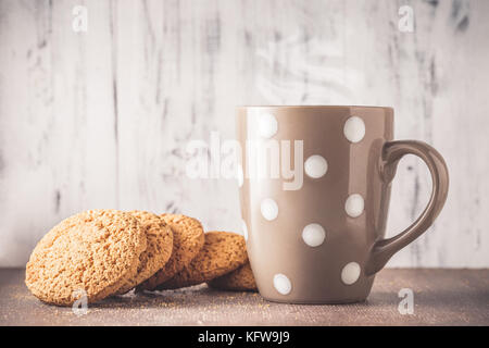 Oat cookies und Polka Dot Becher mit heißem Getränk über Holz- Hintergrund Stockfoto