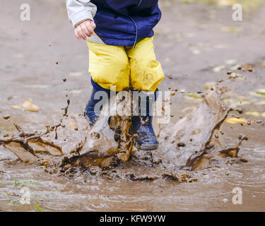 Gerne zwei Jahre alten Jungen springen auf schlammigen Pfützen in Gummistiefel Stockfoto