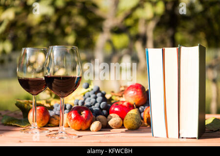 Zwei Gläser Rotwein, Bücher und im Herbst Früchte im Freien auf einem Holztisch auf einem sonnigen Herbst Tag Stockfoto