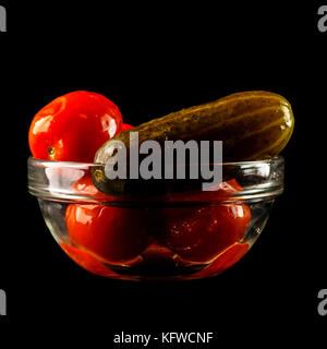 Gesalzene Gurken mit Tomaten im Glas Vase. Eine Schale mit roten Tomaten und Gurken, auf einem schwarzen Hintergrund isoliert Stockfoto