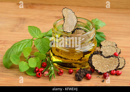 In Scheiben geschnitten Herzförmige schwarze Trüffel in Olivenöl in kleinen Jar und einige frische Gewürze, Basilikum, Oregano, Rosmarin und rotem Pfeffer Stockfoto