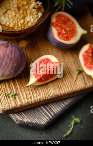 Saftige frische ganze Bild Obst und einem Schnitt Feigen und einer Schale mit Honig in den Waben auf Holz Schneidebrett auf dunkelgrünem Hintergrund Stockfoto