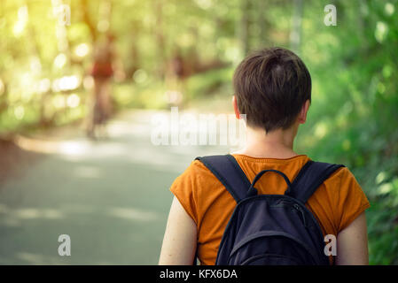 Ansicht der Rückseite des Erwachsenen kaukasischen Frauen mit Rucksack beim Spaziergang im Park auf sonnigen Sommernachmittag. gesunder Lebensstil, Erholung und Natur lovi Stockfoto