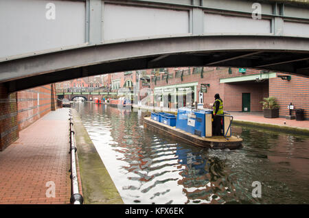 Blick auf einen Kanal und ein Seitenweg in Birmingham mit einem kleinen Lastkahn, der unter einer der Brücken vorbeifährt. Stockfoto