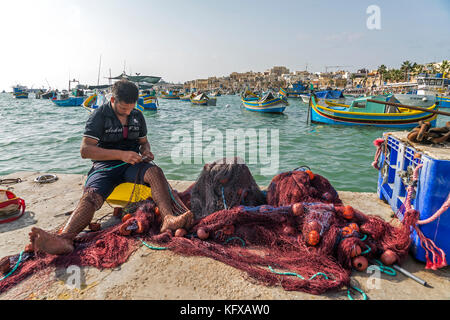 Fischer repariert sein Netz im Hafen von Marsaxlokk, Malta Fischer repariert sein Netz am Hafen in Marsaxlokk, Malta Stockfoto