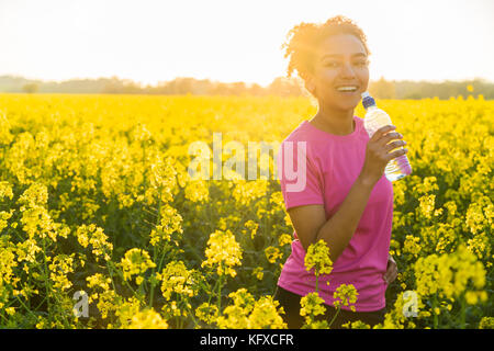 Outdoor Portrait von schönen happy Mixed Race african american girl Teenager weibliche junge Frau Athlet runner Trinkwasser aus einer Flasche in einer fiel
