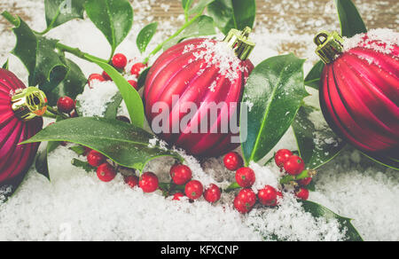 Holly und Weihnachtskugeln im Schnee. Stockfoto