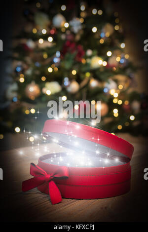 Red christmas gift Box mit magischen funkelt und Star Dust. Unscharfe Weihnachtsbaum im Hintergrund gehalten. Stockfoto