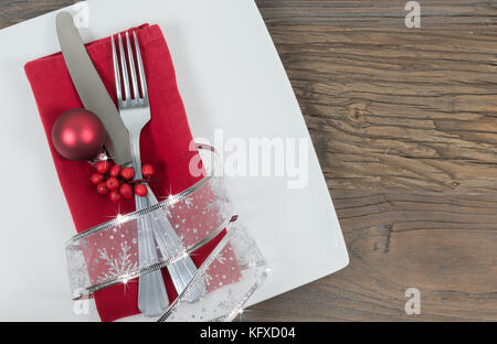 Weihnachtliche Tischunterlage mit silbernem Besteck und roter Serviette auf weißem Teller. Stockfoto