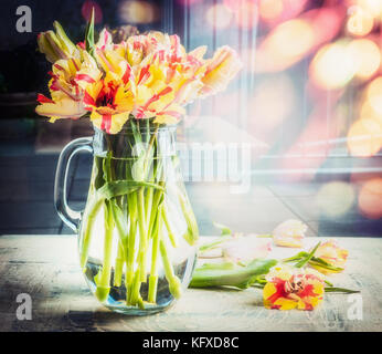 Helle Blumenstrauß aus Tulpen im Glas Kanne auf Tisch in sonniger Frühlingstag Hintergrund mit Bokeh, Vorderansicht Stockfoto