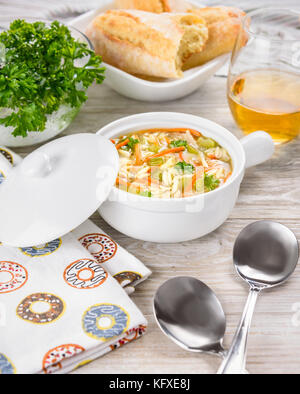 Huhn orzo Suppe in einem weißen Topf auf hölzernen Hintergrund. italienische Suppe mit orzo Pasta. Brot. Glas Wein. Stockfoto
