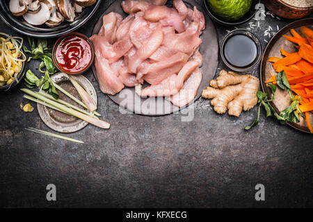 Asiatische Küche Zubereitung mit Zutaten: hähnchenstreifen, schießt, Gemüse und Gewürzen auf dunklen rustikalen Hintergrund, Ansicht von oben, Grenze Stockfoto